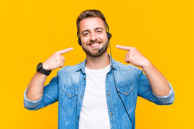 Joven sonriendo con confianza apuntando a su propia sonrisa amplia, actitud positiva, relajada y satisfecha