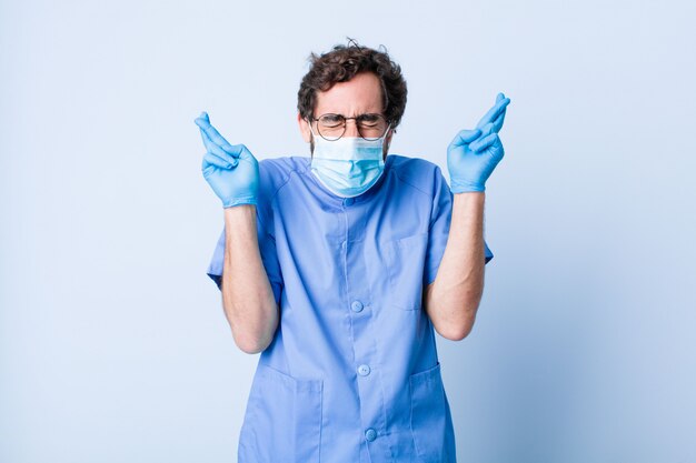 Joven sonriendo y cruzando ansiosamente ambos dedos, sintiéndose preocupado y deseando o esperando buena suerte. concepto de coronavirus