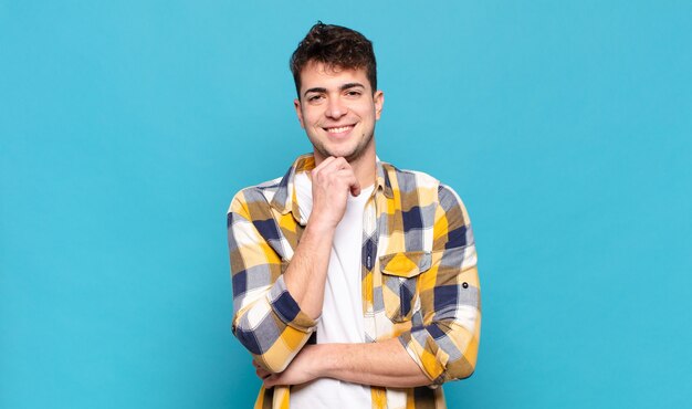 Joven sonriendo, disfrutando de la vida, sintiéndose feliz, amigable, satisfecho y despreocupado con la mano en la barbilla