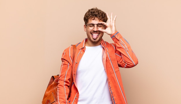 Joven sonriendo felizmente con cara divertida, bromeando y mirando por la mirilla, espiando secretos