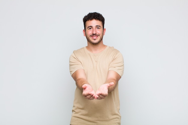 Joven sonriendo felizmente con una mirada amable, segura y positiva, ofreciendo y mostrando un objeto o concepto