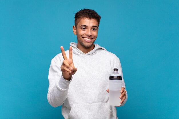 Joven sonriendo y luciendo feliz, despreocupado y positivo, gesticulando victoria o paz con una mano. concepto de deporte