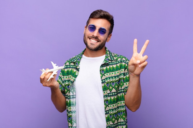 Joven sonriendo y luciendo feliz, despreocupado y positivo, gesticulando victoria o paz con una mano. concepto de vacaciones