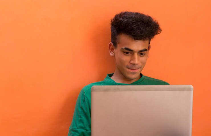 Foto un joven sonriendo mientras habla con alguien en su portátil