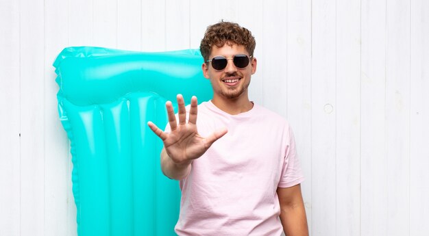 Joven sonriendo y mirando amigable, mostrando el número cinco o quinto con la mano hacia adelante, contando hacia atrás. concepto de vacaciones