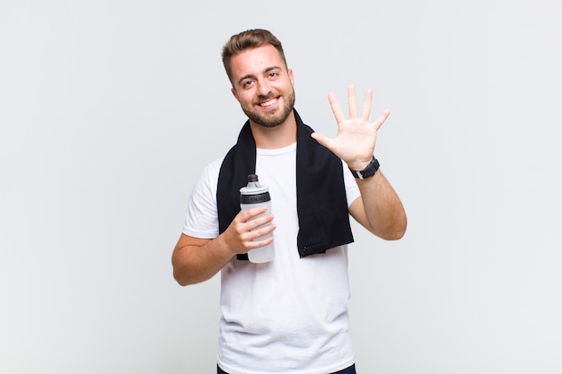 Joven sonriendo y mirando amigable, mostrando el número cinco o quinto con la mano hacia adelante, contando hacia atrás