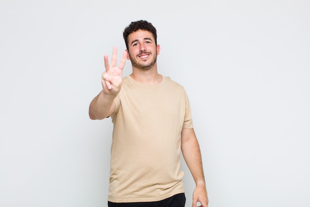 Joven sonriendo y mirando amigable, mostrando el número uno o primero con la mano hacia adelante, contando hacia atrás