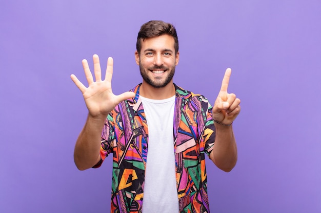 Joven sonriendo y mirando amistosamente, mostrando el número seis o sexto con la mano hacia adelante, contando hacia atrás