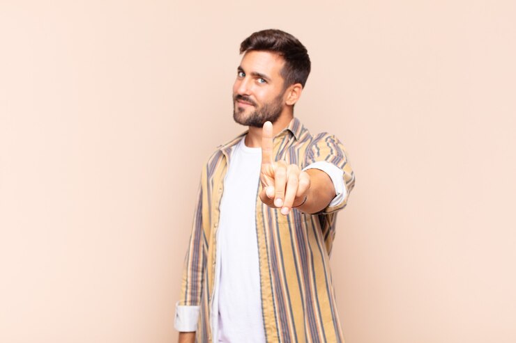 Foto joven sonriendo con orgullo y confianza haciendo la pose número uno triunfalmente, sintiéndose como un líder