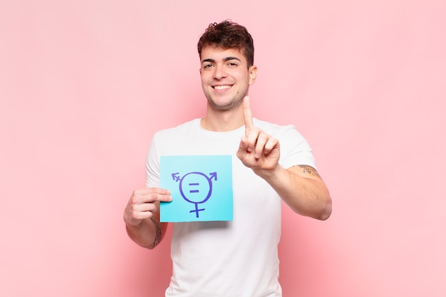 Joven sonriendo con orgullo y confianza haciendo la pose número uno triunfalmente, sintiéndose como un líder