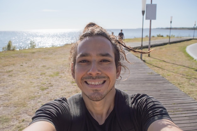 Joven sonriendo en la playa tomándose un selfie con el mar de fondo