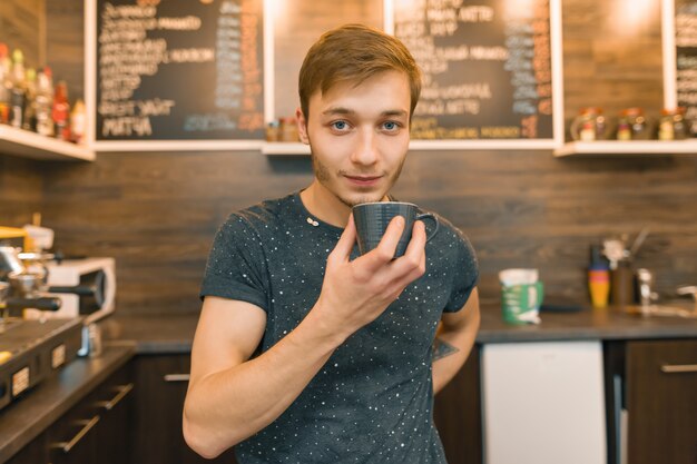 Joven sonriente barista masculino bebe café en la cafetería.