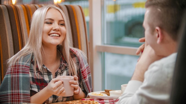 Una joven sonriente bebe café y habla con su novio en el café
