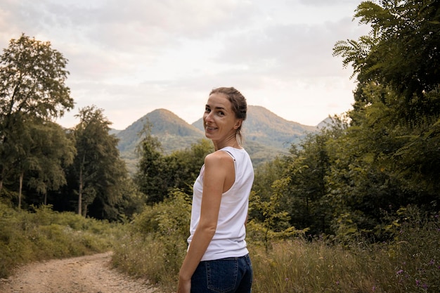 Foto una joven sonriente en el bosque con el telón de fondo de las montañas