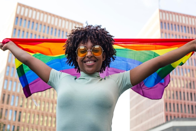 Un joven sonriente con cabello afro agitando la bandera del orgullo LGBTI