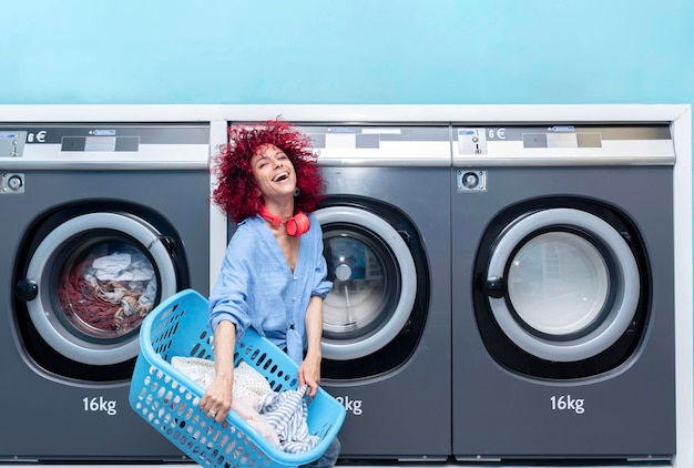 Una joven sonriente con cabello afro rojo lavando ropa en una lavandería automática azul