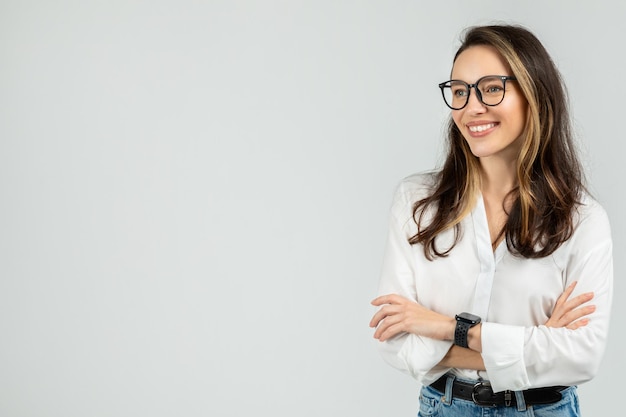 Foto una joven sonriente con cabello moreno y gafas se para con los brazos cruzados