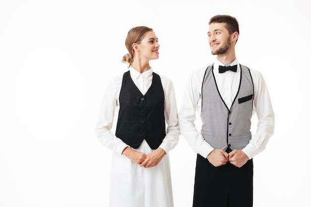 Joven sonriente camarero y bonita camarera en camisas blancas y chalecos felizmente