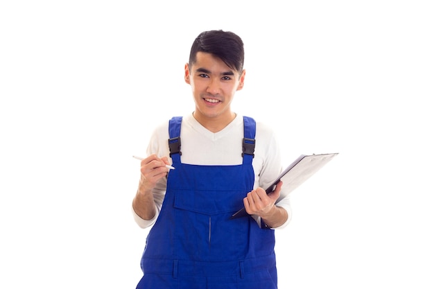 Joven sonriente con camisa blanca y mono azul sosteniendo un bolígrafo blanco y una carpeta negra