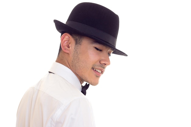 Joven sonriente con camisa blanca con pajarita negra y sombrero negro sobre fondo blanco en el estudio