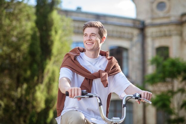 Un joven sonriente con una camiseta blanca en una bicicleta