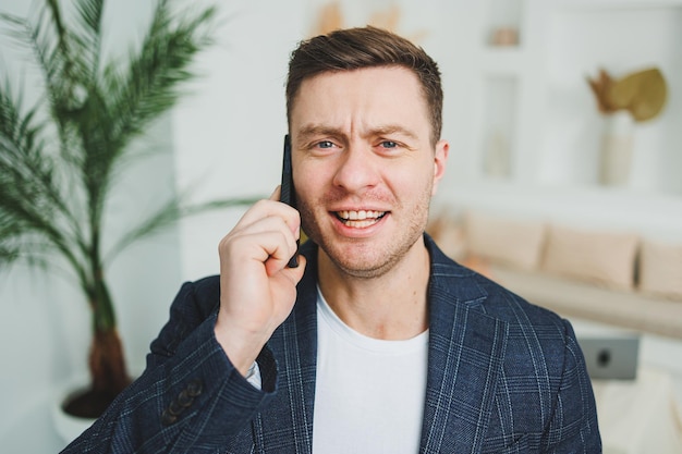 Un joven sonriente con una chaqueta está hablando por teléfono Emociones de risa por hablar por teléfono Un hombre exitoso trabaja remotamente por teléfono