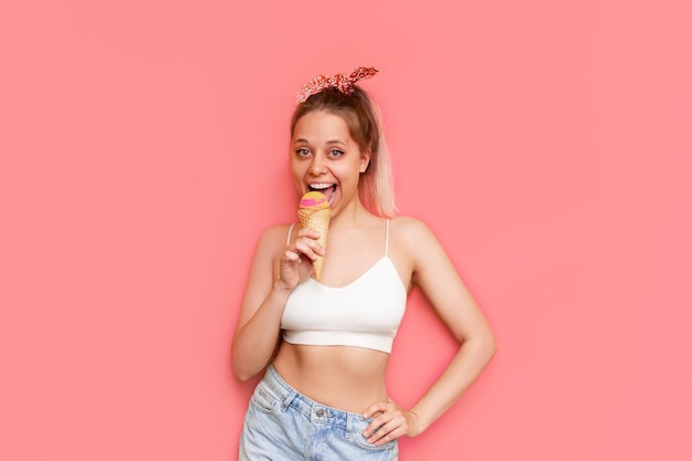 Una joven sonriente come sorbete de helado de frutas en un cono de gofre aislado en un fondo rosa