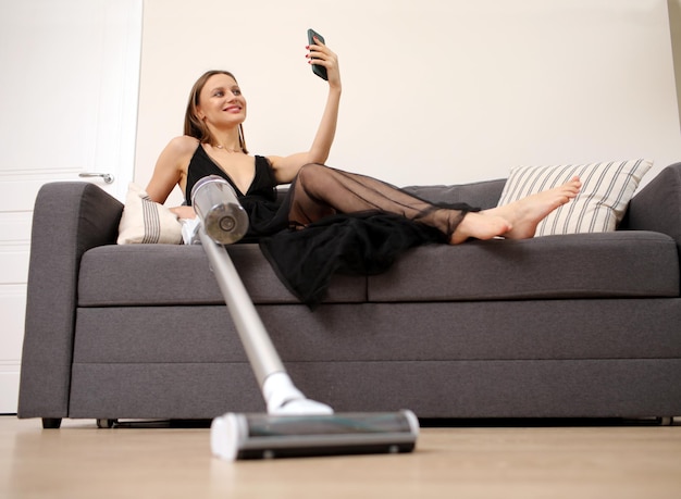 Una joven sonriente con un elegante vestido largo y negro está sentada en el sofá y usando un teléfono celular