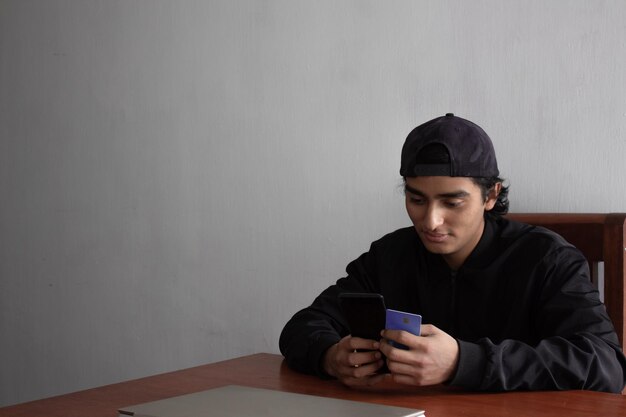 Joven sonriente y emocionado haciendo una compra en línea con su tarjeta de crédito en su teléfono inteligente