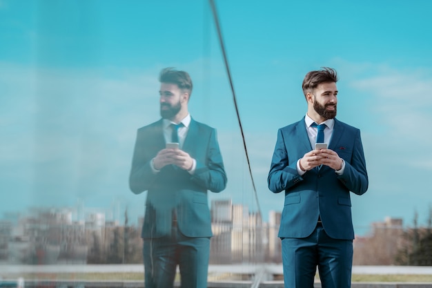 Joven sonriente exitoso empresario caucásico barbudo en ropa formal de pie en la azotea