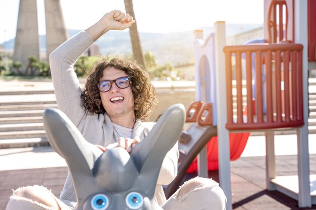 Joven sonriente feliz columpio en el patio de recreo