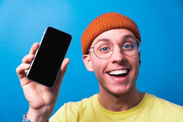 Foto joven sonriente con gafas que muestra una aplicación de teléfono inteligente con pantalla limpia para maqueta