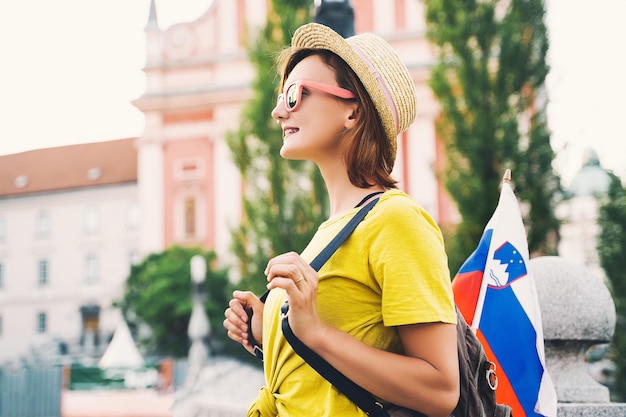 Joven sonriente con gafas de sol con bandera eslovena en la plaza central de Ljubljana Mujer turista y bandera eslovena en el fondo de la arquitectura de la ciudad Viajar estudio de vida en Eslovenia Europa