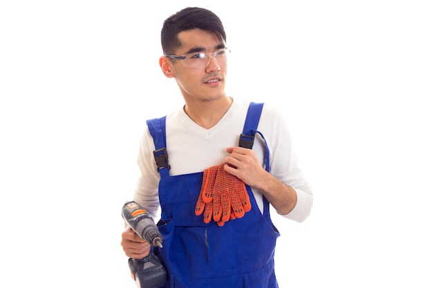 Joven sonriente con guantes naranjas y gafas protectoras con destornillador eléctrico