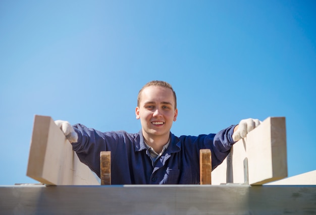 Un joven sonriente con guantes y ropa de trabajo está construyendo un techo.