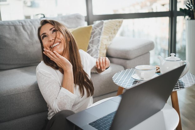 Foto joven sonriente haciendo videollamadas en su tiempo libre en su casa con una laptop.