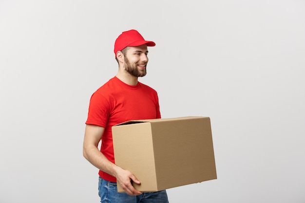 Joven sonriente hombre de entrega logística en uniforme rojo sosteniendo la caja en blanco