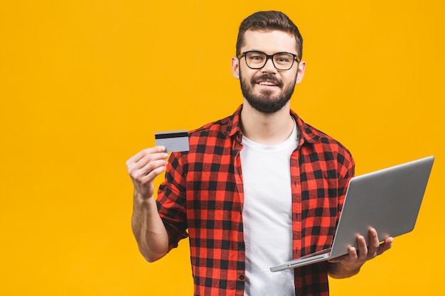 Joven sonriente con laptop y tarjeta de crédito