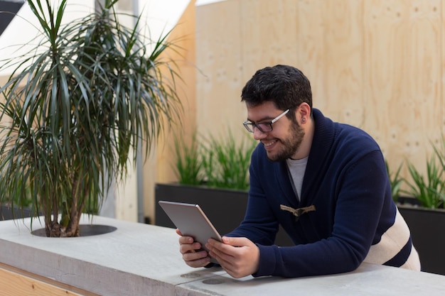 Joven sonriente leyendo tableta digital por planta en la mesa