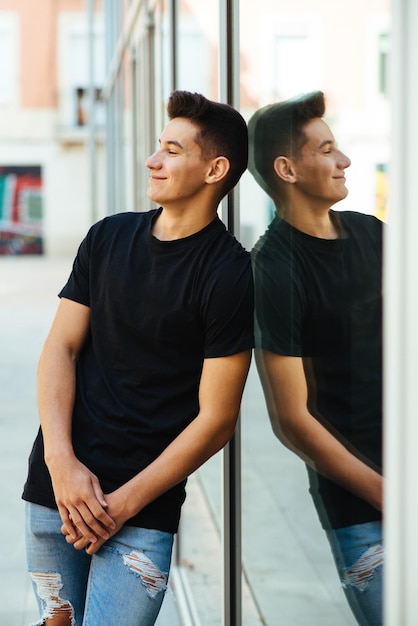 Foto un joven sonriente mirando hacia otro lado mientras está de pie contra la ventana