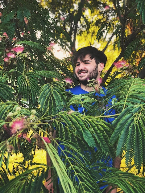 Foto un joven sonriente mirando hacia otro lado mientras está de pie en medio de las plantas en el parque