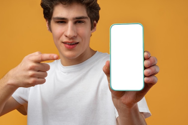 Foto un joven sonriente mostrando una maqueta de pantalla blanca en blanco de su teléfono móvil a la cámara