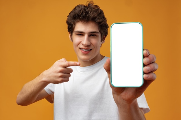Un joven sonriente mostrando una maqueta de pantalla blanca en blanco de su teléfono móvil a la cámara