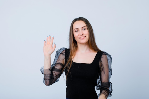 Una joven sonriente muestra un gesto de saludo levantando la mano sobre fondo blanco