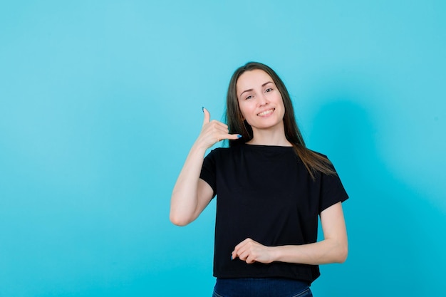 Una joven sonriente muestra un gesto de teléfono con fondo azul