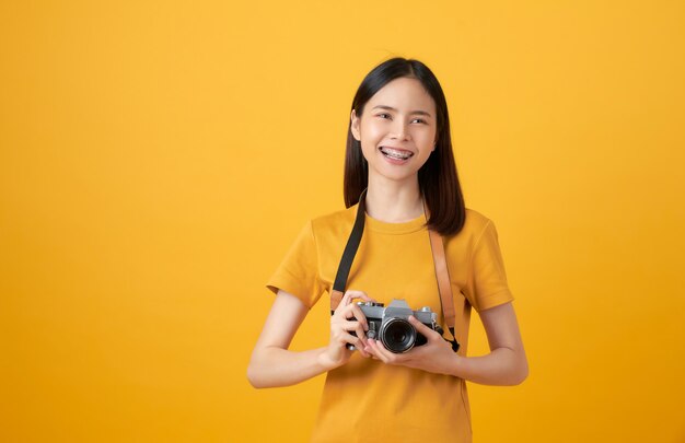 Joven sonriente mujer asiática turista sosteniendo la cámara y mirando para copiar spac