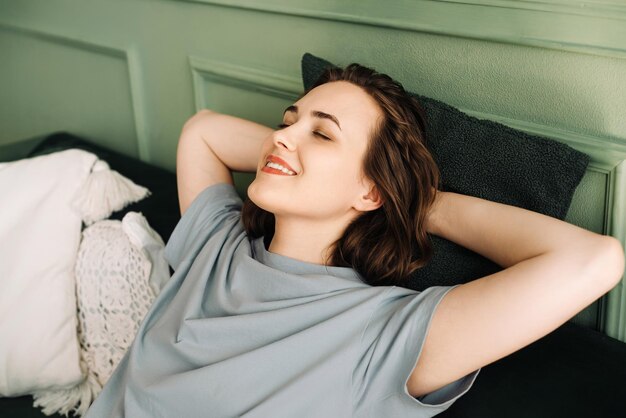 Una joven sonriente con los ojos cerrados está acostada en un sofá disfrutando de un poco de descanso y sueño Sereni