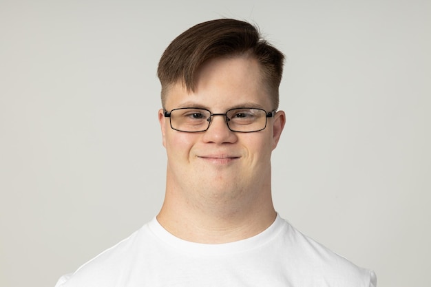 Un joven sonriente con parálisis cerebral con gafas y una camiseta blanca posa para la cámara concepto del Día Mundial de las Enfermedades Genéticas