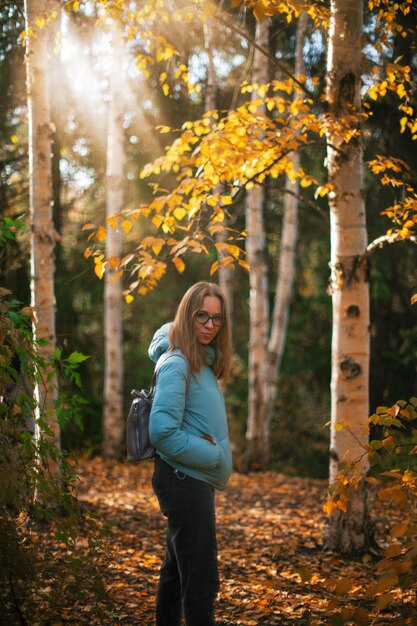 Una joven sonriente de pie junto a un árbol en el bosque durante el otoño