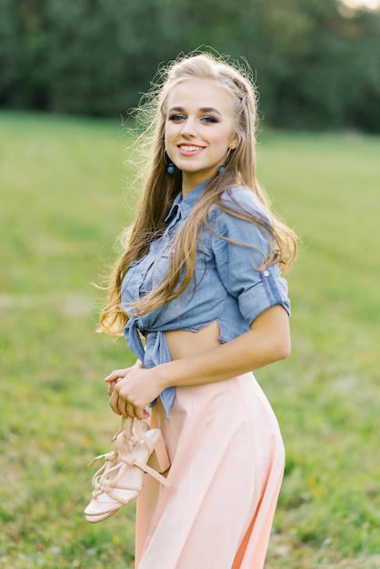 Una joven sonriente con ropa casual camina por el parque, tiene zapatos en las manos, es libre y feliz, el concepto de libertad y juventud.